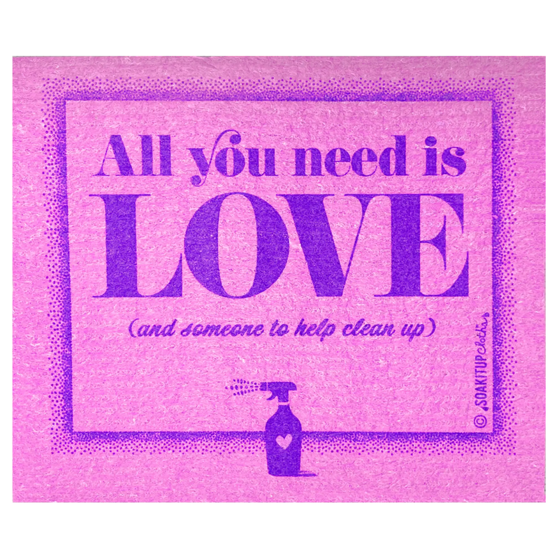 A Swedish dishcloth with graphic print in a pink and purple color scheme, featuring the text 'All you need is LOVE (and someone to help clean up)' in stylized lettering, with a small illustration of a spray bottle at the bottom.
