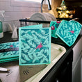 Load image into Gallery viewer, Teal and pink holiday reusable swedish sponge with cardinal bird and pine branch design from soak it up clards greeting card turns
