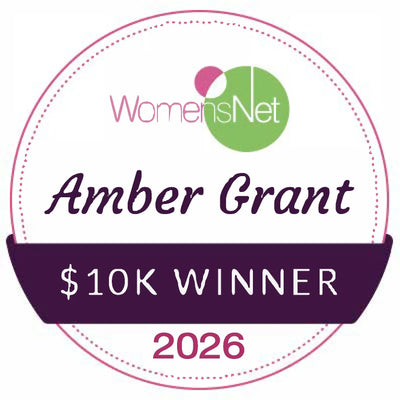 A circular badge with a dotted border, featuring the womensnet logo and text that reads ’amber grant $10k winner 2026’’ in purple and pink.
