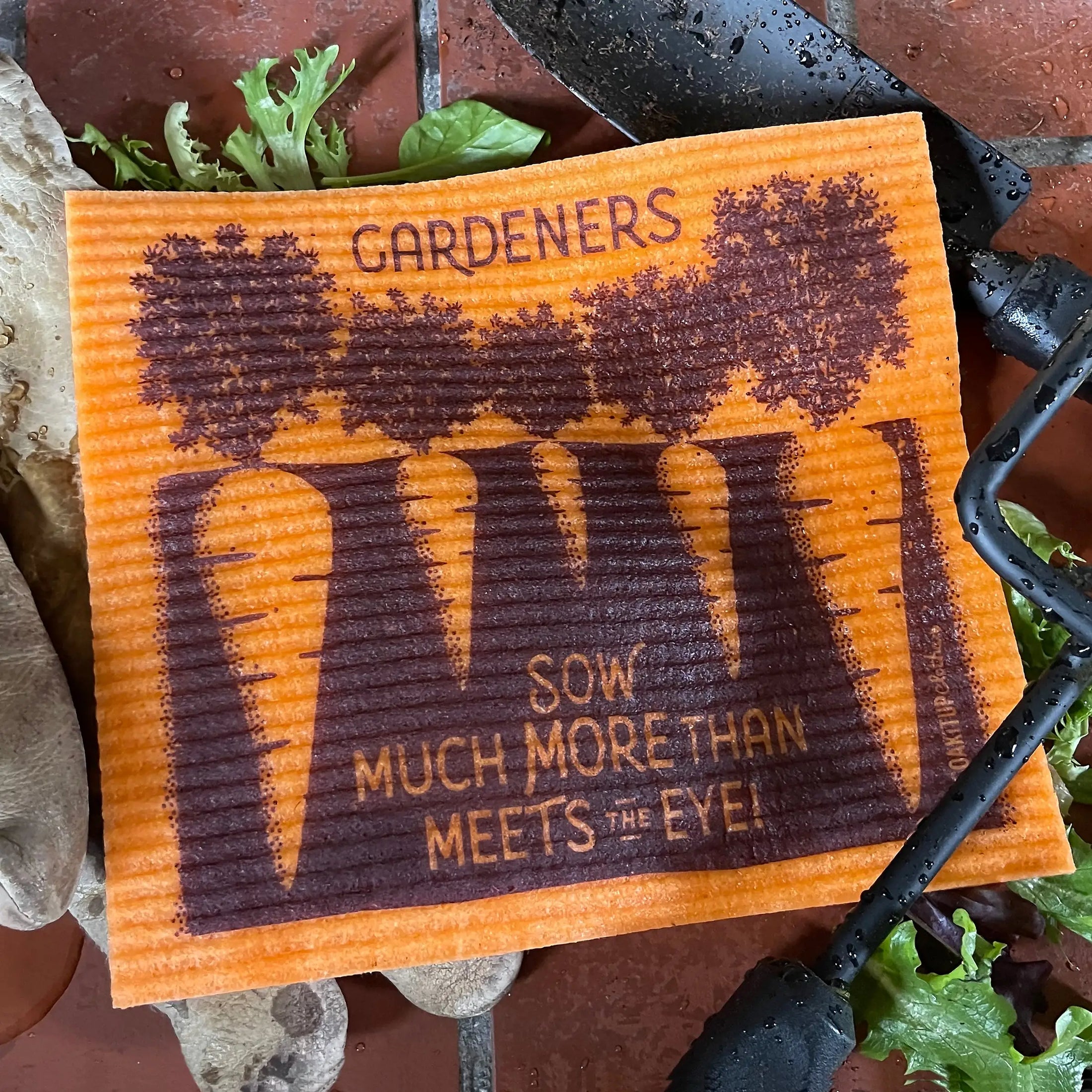 Orange corrugated eye swedish dishcloth with dark brown carrot and tree design and gardeners sow text by soak iT up