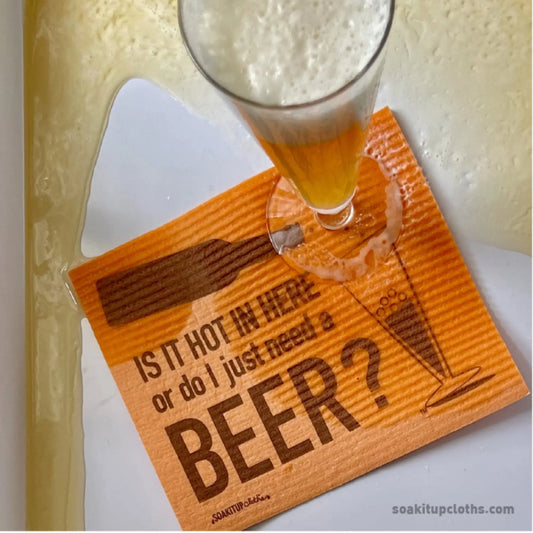 Orange Swedish dishcloth with a glass of beer and text 'Is it hot in here or do I just need a BEER?' on a white surface.