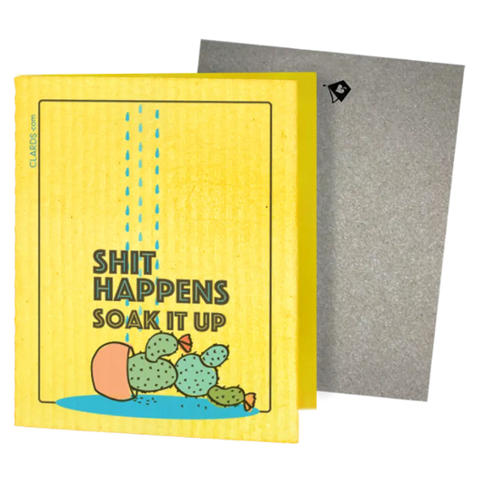 A yellow rectangular card or box with a humorous printed design reading 'SHIT HAPPENS SOAK IT UP' above a cartoon cactus in a puddle. Greeting turns into cleaning cloths